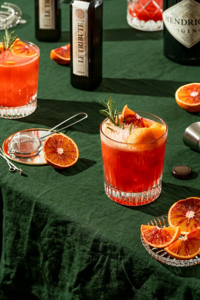 Blood orange cocktails with rosemary sprigs on a dark green linen tablecloth