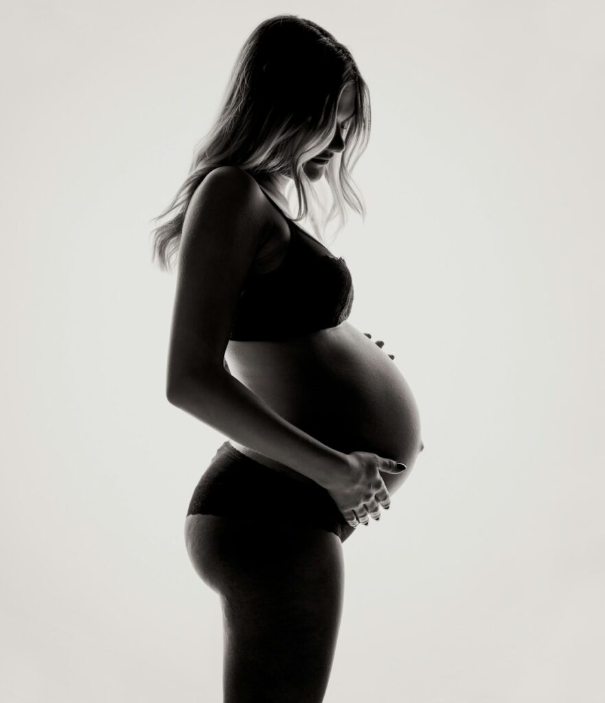 A pregnant woman in silhouette holding her belly against a bright white background