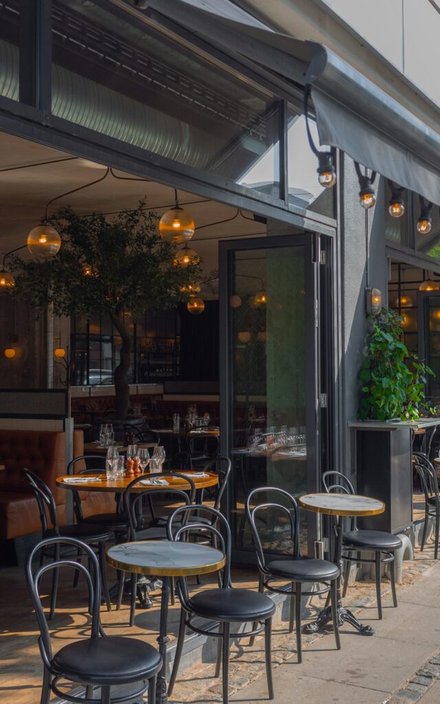 Tables and chairs on a restaurant patio with an open glass storefront
