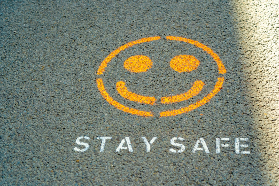 An orange spray-painted smiley face and the text STAY SAFE on grey asphalt