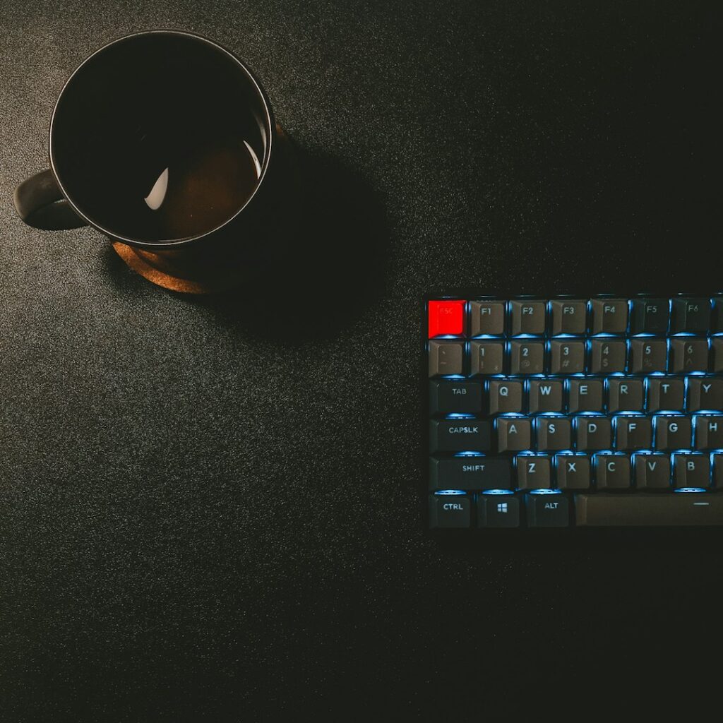 A black coffee mug and a mechanical keyboard with blue backlighting on a desk