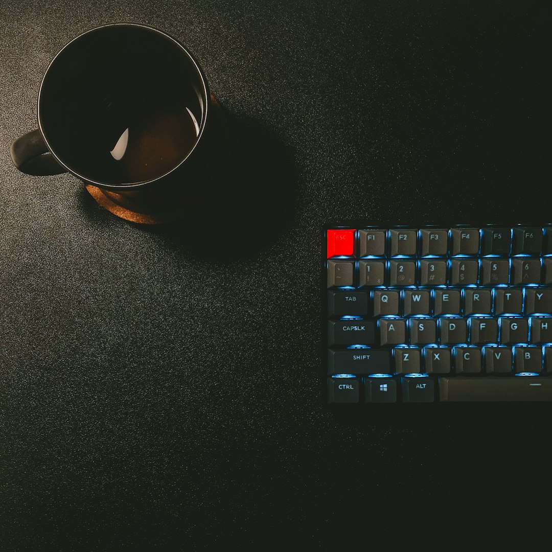 A black coffee mug and a mechanical keyboard with blue backlighting on a desk