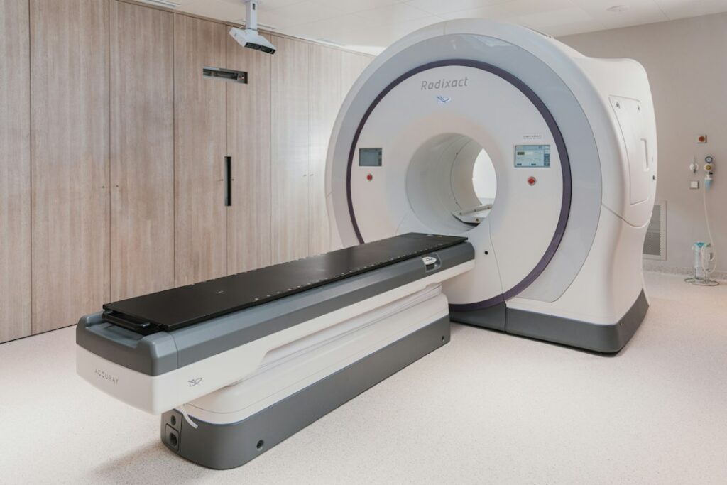 A white medical radiation therapy machine with a black patient table in a clinic